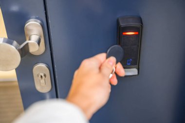 Evin duvarına monte edilmiş bir giriş sistemi okuyucusuyla bir binaya girmek için elektrikli kilit anahtarı kullanan birini kapat. Yüksek kalite fotoğraf