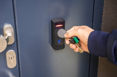 Evin duvarına monte edilmiş bir giriş sistemi okuyucusuyla bir binaya girmek için elektrikli kilit anahtarı kullanan birini kapat. Yüksek kalite fotoğraf