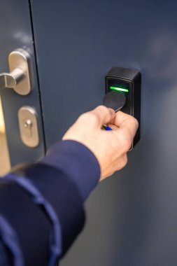 Evin duvarına monte edilmiş bir giriş sistemi okuyucusuyla bir binaya girmek için elektrikli kilit anahtarı kullanan birini kapat. Yüksek kalite fotoğraf
