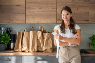 Mutfakta içi yiyecek dolu kağıt torbaların yanındaki dükkandan alınmış fişi olan genç bir kadın. Yiyecekler internetten sipariş edildi ve kuryeyle teslim edildi. Yüksek kalite fotoğraf
