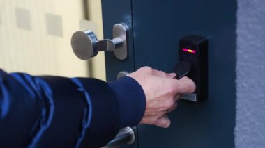 Evin duvarına monte edilmiş bir giriş sistemi okuyucusuyla bir binaya girmek için elektrikli kilit anahtarı kullanan birini kapat. Yüksek kalite 4k görüntü