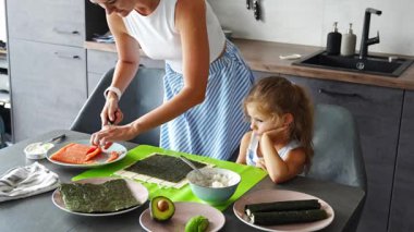 Genç bir anne ve küçük kızı mutfaktaki masada suşi yapıyor. Yüksek kalite 4k görüntü