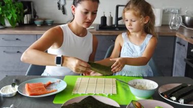 Genç bir anne ve küçük kızı mutfaktaki masada suşi yapıyor. Yüksek kalite 4k görüntü