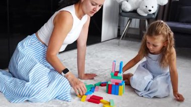 Annesiyle birlikte evde Jenga masa oyunu oynayan küçük bir kız renkli bloklarla ahşap kule inşa ediyor. Yüksek kalite 4k görüntü