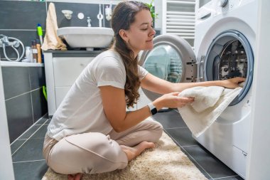 Çamaşır makinesinin içine çamaşır sokan genç bir kadın. Yüksek kalite fotoğraf