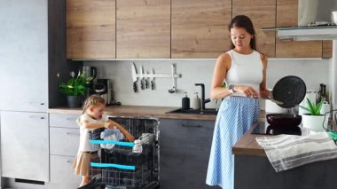 Küçük bir kız, annesi yemek pişirirken temiz seramik tabakları bulaşık makinesinden çıkarıyor. Ev ve kullanışlı teknoloji konsepti. Yüksek kalite 4k görüntü