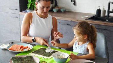 Genç bir anne ve küçük kızı mutfaktaki masada suşi yapıyor. Yüksek kalite 4k görüntü