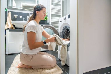 Çamaşır makinesinin içine çamaşır sokan genç bir kadın. Yüksek kalite fotoğraf