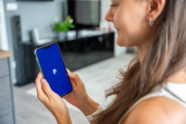 Prag, Çek Cumhuriyeti - 2 Mayıs 2024: Sohbet uygulaması PayPal ile iPhone 'u elinde tutan kadın, iş yeri için mobil uygulama kullanıyor. Yüksek kalite fotoğraf