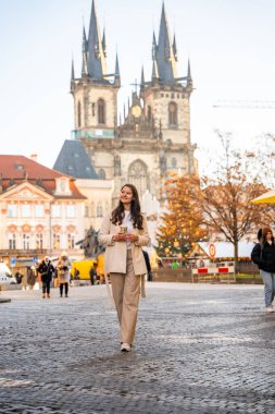 Prag, Çek Cumhuriyeti - 4 Aralık 2024: Çek Cumhuriyeti 'nin Prag kentindeki Old Town Square' de Noel tatilinde Tyn tapınağı ve Noel ağacının yanındaki genç kadın. Yüksek kalite fotoğraf