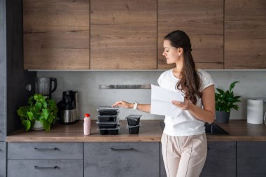Kilo kaybı için sağlıklı beslenme planı olan genç bir kadın, günlük hazır yemek menüsü teslimatı. Cep telefonu uygulaması ile sipariş edilen yemek. Tabakla dengeli porsiyon. Pişirme öncesi. Yüksek kalite fotoğraf