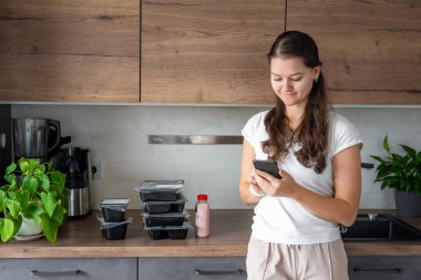 Kilo kaybı için sağlıklı beslenme planı olan genç bir kadın, günlük hazır yemek menüsü teslimatı. Telefonda yemek izleme uygulaması kullanan bir kadın. Tabakla dengeli porsiyon. Pişirme öncesi. Yüksek kalite fotoğraf