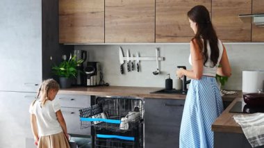 Bir kadın bulaşık makinesinden temiz seramik tabakları kaldırıyor, kızı yardım ediyor. Ev ve kullanışlı teknoloji konsepti. Yüksek kalite 4k görüntü