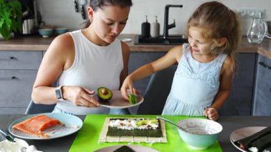 Genç bir anne ve küçük kızı mutfaktaki masada suşi yapıyor. Yüksek kalite 4k görüntü