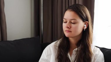 Genç bir kadın kulağına beyaz, modern, kablosuz bir kulaklık taktı ve müziği açtı. Teknoloji konsepti. Yüksek kalite 4k görüntü