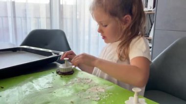 Küçük kız mutfaktaki masada oturmuş ev yapımı kurabiyeler yapıyor. Yüksek kalite 4k görüntü