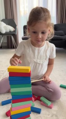 Evde masa oyunu oynayan küçük bir kız, ahşap kuleden renkli bloklar alıyor. dikey video. Yüksek kalite 4k görüntü