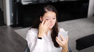 Evde oturma odasında otururken video konferans görüşmesine başlamadan önce makyajını tazeleyen genç bir kadın. Yüksek kalite 4k görüntü