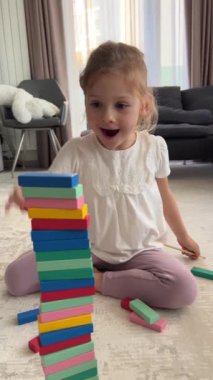 Evde masa oyunu oynayan küçük bir kız, ahşap kuleden renkli bloklar alıyor. dikey video. Yüksek kalite 4k görüntü