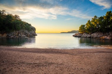 Wild beach near Sveti Stefan at sunset, near Budva, Montenegro. Waves and rocks at sunset lights. High quality photo clipart