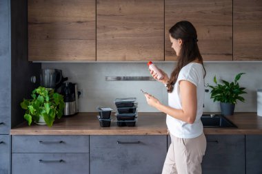 Kilo kaybı için sağlıklı beslenme planı olan genç bir kadın, günlük hazır yemek menüsü teslimatı. Telefonda yemek izleme uygulaması kullanan bir kadın. Tabakla dengeli porsiyon. Pişirme öncesi. Yüksek kalite fotoğraf