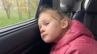 Küçük kız şehrin içinden geçerken düşünceli bir şekilde arabanın camından dışarı bakar. Yüksek kalite 4k görüntü