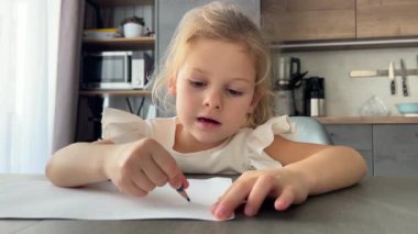Evde masada oturan kalemlerle resim yapan küçük bir kız. Yüksek kalite 4k görüntü