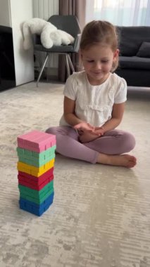 Evde masa oyunu oynayan küçük bir kız, ahşap kuleden renkli bloklar alıyor. dikey video. Yüksek kalite 4k görüntü