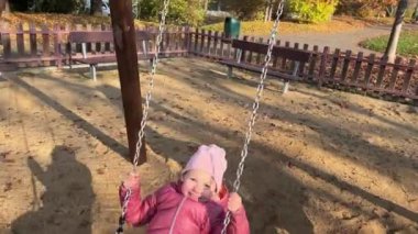 Sonbahar zamanı şehir parkında oyun parkında eğlenen küçük kız. Salıncakta sallanan çocuk. Yüksek kalite 4k görüntü