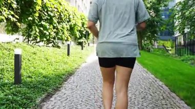 Yaz parkında parkta canlı yürüyüş yapan genç bir kadın. Spor salonundaki kadın dışarıda koşuyor. Sabah koşusu kavramı. Yüksek kalite 4k görüntü
