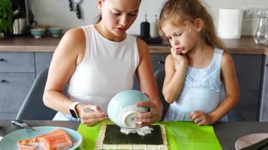 Genç bir anne ve küçük kızı mutfaktaki masada suşi yapıyor. Yüksek kalite 4k görüntü