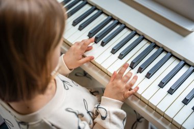 Beyaz piyano sentezleyicili kız için ev müziği dersi. Erken gelişim kavramı: müzik öğrenmek motor becerileri, işitme ve zekayı geliştirir, çocukluktan itibaren yaratıcılığı teşvik eder.. 