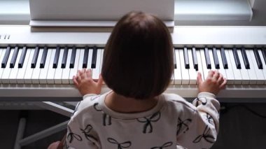 Beyaz piyano sentezleyicili kız için ev müziği dersi. Erken gelişim kavramı: müzik öğrenmek motor becerileri, işitme ve zekayı geliştirir, çocukluktan itibaren yaratıcılığı teşvik eder.. 