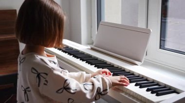 Beyaz piyano sentezleyicili kız için ev müziği dersi. Erken gelişim kavramı: müzik öğrenmek motor becerileri, işitme ve zekayı geliştirir, çocukluktan itibaren yaratıcılığı teşvik eder.. 