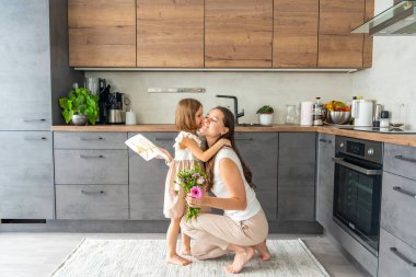 Küçük kız bir buket çiçek veriyor ve ev mutfağında annesine çiziyor. Anneler günü, doğum günü ya da 8. Uluslararası Kadınlar Günü konsepti. Yüksek kalite fotoğraf