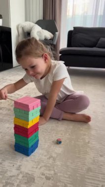 Evde masa oyunu oynayan küçük bir kız, ahşap kuleden renkli bloklar alıyor. dikey video. Yüksek kalite 4k görüntü