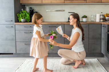 Küçük kız bir buket çiçek veriyor ve ev mutfağında annesine çiziyor. Anneler günü, doğum günü ya da 8. Uluslararası Kadınlar Günü konsepti. Yüksek kalite fotoğraf