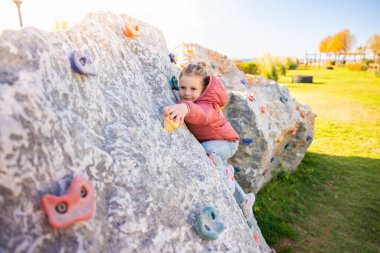 Oyun parkında yapay bir tırmanma duvarına tırmanan küçük bir kız güç ve koordinasyon geliştiriyor. Yüksek kalite fotoğraf