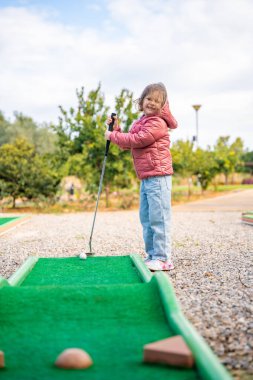 Küçük kız dışarıda mini golf oynuyor. Çocuk bahar zamanı yeni aktivitelerle eğleniyor. Aile tatilleri ya da tatil köyleri. Yüksek kalite fotoğraf
