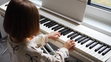 Beyaz piyano sentezleyicili kız için ev müziği dersi. Erken gelişim kavramı: müzik öğrenmek motor becerileri, işitme ve zekayı geliştirir, çocukluktan itibaren yaratıcılığı teşvik eder.. 