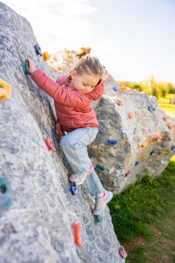 Oyun parkında yapay bir tırmanma duvarına tırmanan küçük bir kız güç ve koordinasyon geliştiriyor. Yüksek kalite fotoğraf