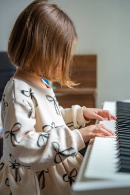 Beyaz piyano sentezleyicili kız için ev müziği dersi. Erken gelişim kavramı: müzik öğrenmek motor becerileri, işitme ve zekayı geliştirir, çocukluktan itibaren yaratıcılığı teşvik eder.. 