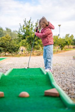 Küçük kız dışarıda mini golf oynuyor. Çocuk bahar zamanı yeni aktivitelerle eğleniyor. Aile tatilleri ya da tatil köyleri. Yüksek kalite fotoğraf