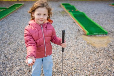 Elinde mini golf topu tutan küçük kızın portresi. Küçük kız dışarıda mini golf oynuyor. Aile tatilleri ya da tatil köyleri. Yüksek kalite fotoğraf
