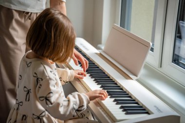 Beyaz piyano sentezleyicili kız için öğretmenle müzik dersi. Erken gelişim kavramı: müzik öğrenmek motor becerileri, işitmeyi, zekayı, çocukluktan yaratıcılığı teşvik eder. 
