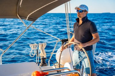 Genç kaptan dümende duruyor ve deniz yolculuğu sırasında bir yelkenliyi kontrol ediyor. Yüksek kalite fotoğraf