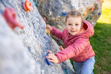 Oyun parkında yapay bir tırmanma duvarına tırmanan küçük bir kız güç ve koordinasyon geliştiriyor. Yüksek kalite fotoğraf
