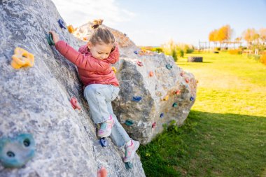 Oyun parkında yapay bir tırmanma duvarına tırmanan küçük bir kız güç ve koordinasyon geliştiriyor. Yüksek kalite fotoğraf