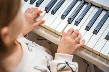 Beyaz piyano sentezleyicili kız için ev müziği dersi. Erken gelişim kavramı: müzik öğrenmek motor becerileri, işitme ve zekayı geliştirir, çocukluktan itibaren yaratıcılığı teşvik eder.. 