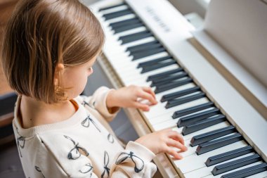 Beyaz piyano sentezleyicili kız için ev müziği dersi. Erken gelişim kavramı: müzik öğrenmek motor becerileri, işitme ve zekayı geliştirir, çocukluktan itibaren yaratıcılığı teşvik eder.. 